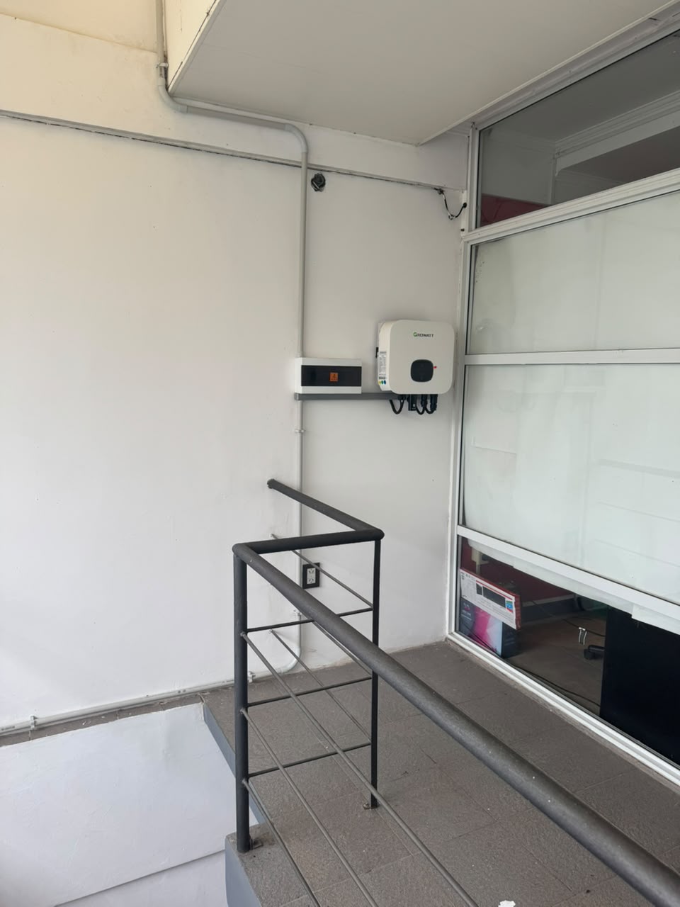 Inversor solar Growatt instalado en una pared exterior junto a una barandilla y una ventana